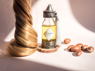 Curll hair of golden hair and decorative bottle with iron embossed in traditional Moroccan style with precious Moroccan argan oil and nuts ander natural lighting of sun with hadows frame