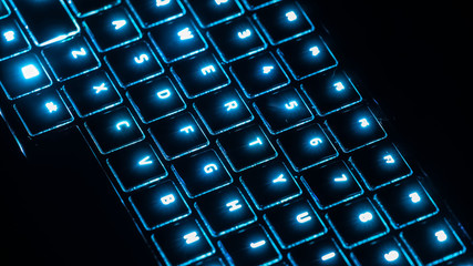 A closeup of an illuminating neon blue keyboard from a workplace laptop computer in low light scene.