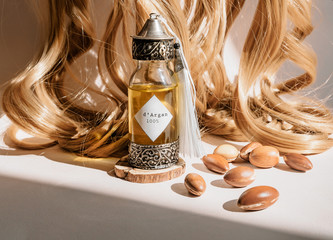 Curls of golden hair and decorative bottle with iron embossed in traditional Moroccan style with precious Moroccan argan oil and nuts ander natural lighting of sun with hadows frame