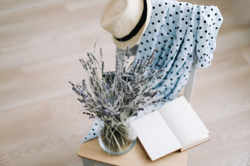 Creative flat lay top view. Blue dress, sun hat, flowers in a vase and a book on wooden  background. Summer holiday concept. 