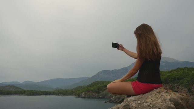 Female tourist sitting on a rock on clear sky and calm sea background
