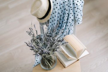 Creative flat lay top view. Blue dress, summer hat, flowers in a vase and a book on wooden  background. Summer holiday concept. 