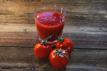 tomatoes and tomato smoothies in a glass on a wooden background.