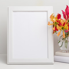 Composition from a decorative wooden frame and red and yellow flowers of Glorios in a glass vase on a white shelf