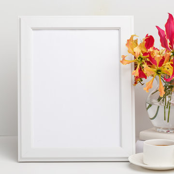 Composition from a decorative wooden frame and red and yellow flowers of Glorios in a glass vase on a white shelf