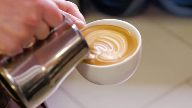Professional barista making pouring stream milk with beautiful latte art pattern, top view.