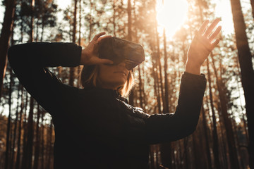 Woman in forest with virtual reality headset looking straight and trying to touch something with her hand