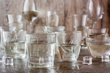 Many glasses of water splashed with drops and pieces of ice on a gray table