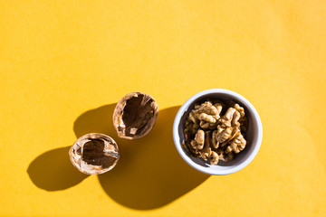 Walnut kernels in a bowl and walnut shells on a yellow table. Top view. Hard light
