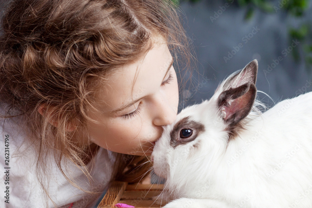 Wall mural little girl playing with real rabbit. child and white bunny on easter on flower background. kid kiss