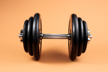 Professional dumbbell and weight plates over beige background. Black metal dumbbell with chrome...