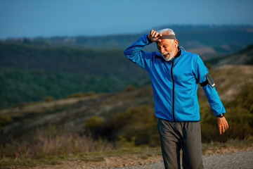 Senior athletic man catching his breath after a run in nature.