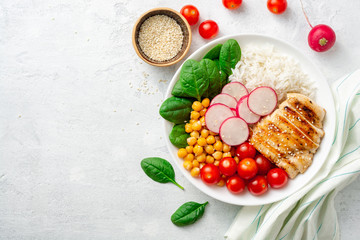 Healthy buddha bowl with spinach, tomato, chickpea, rice, radish and grilled chicken on concrete background. Top view. Copy space.