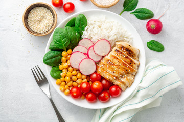 Healthy buddha bowl with spinach, tomato, chickpea, rice, radish and grilled chicken on concrete...