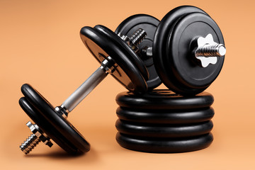 Professional dumbbell and weight plates over beige background. Black metal dumbbell with chrome silver handle. Gym equipment. Fitness concept.