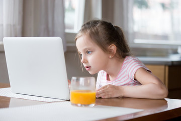 Little girl busy playing computer in kitchen at home