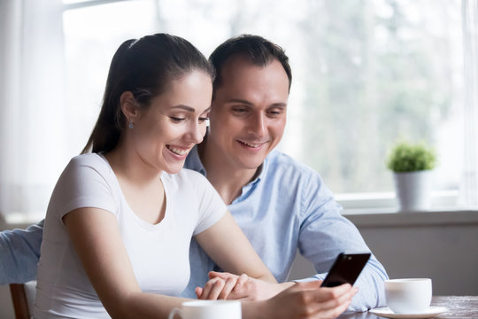 Smiling couple reading funny message on phone at home