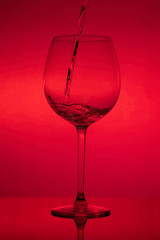 Filling the glass, pouring wineglass on red background