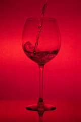 Filling the glass, pouring wineglass on red background