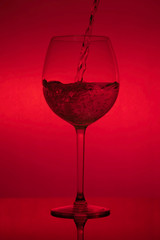 Filling the glass, pouring wineglass on red background