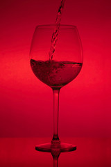Filling the glass, pouring wineglass on red background
