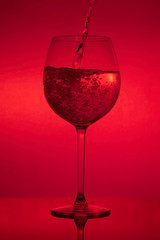 Filling the glass, pouring wineglass on red background