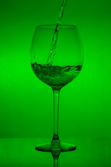 Filling the glass, pouring wineglass on green background