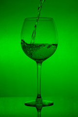 Filling the glass, pouring wineglass on green background