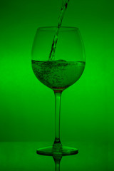 Filling the glass, pouring wineglass on green background