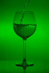Filling the glass, pouring wineglass on green background