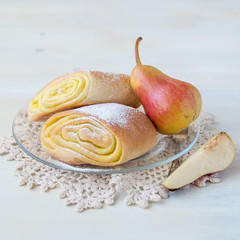 Sweet pastries. Fresh homemade buns with fruit filling and the ripe juicy pears on a round plate on a light wooden table. Selective focus.