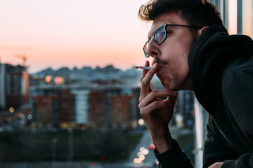 Young man smoking a cigarette on the balcony in sunset