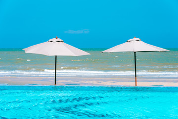 Umbrella and chair around swimming pool neary sea ocean beach with blue sky and white cloud