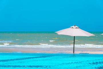Umbrella and chair around swimming pool neary sea ocean beach with blue sky and white cloud