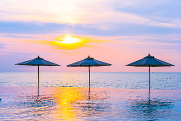 Umbrella and chair around swimming pool neary sea ocean beach at sunrise or sunset time