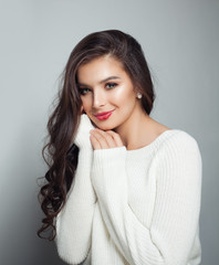 Pretty woman wearing white sweater. Perfect female model with long curly hair and makeup