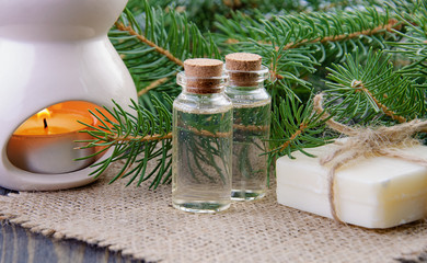 Two bottles of spruce essential oil, natural soap and fir branches behind on linen napkin.