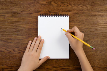 Boy holds pencil in hand and writes into notebook with copyspace. Top view.