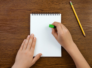 The boy holds the eraser in his hand and erases in white blank notebook. Top view on wooden...