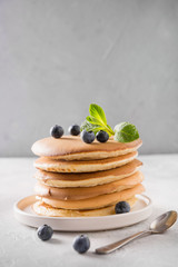 Stack of pancakes with fresh blueberry and mint on light background.