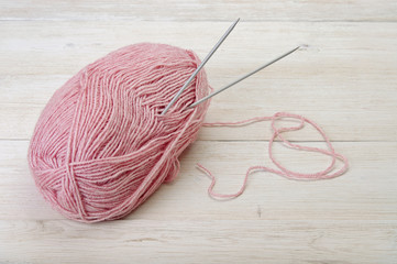 Hank of pink yarn and needles on light wood. Knitting background.