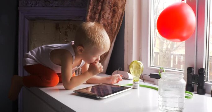 Two Funny blond children with red ball plays computer games on ttablet. Modern communications, tablet, smartphone, computer.
