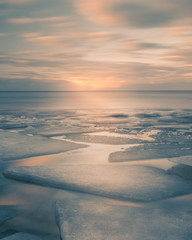 Sunset on the Kyiv Sea at wintertime with broken ice cracks in Golden Hour with beautiful clouds. Pack Ice builds up the icebergs. Ukraine