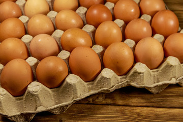 Raw chicken eggs in cardboard pack on wooden table