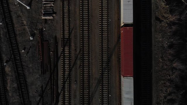 Aerial view of a large train on the rails next to the river. The camera flies over a long train of tanks standing on the rails