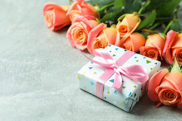 Fresh orange roses with gift and space for text on grey background, closeup
