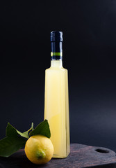 Lemoncello in a bottle on a black background, Traditional Italian liqueur from lemons. Alcohol yellow and fresh lemon with green leaves. Place for text
