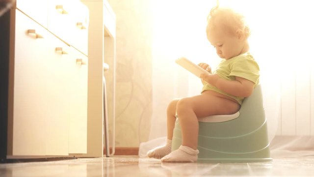 Funny focused baby uses smartphone while sitting on the potty