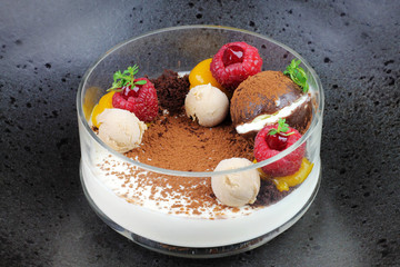 Chocolate dessert with mango and raspberry fruit on black plate.