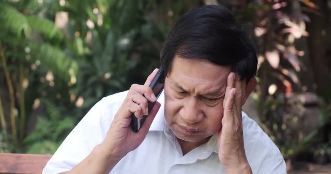 Senior man sitting on park bench using mobile phone. Asian man, Talking on phone and confuse.